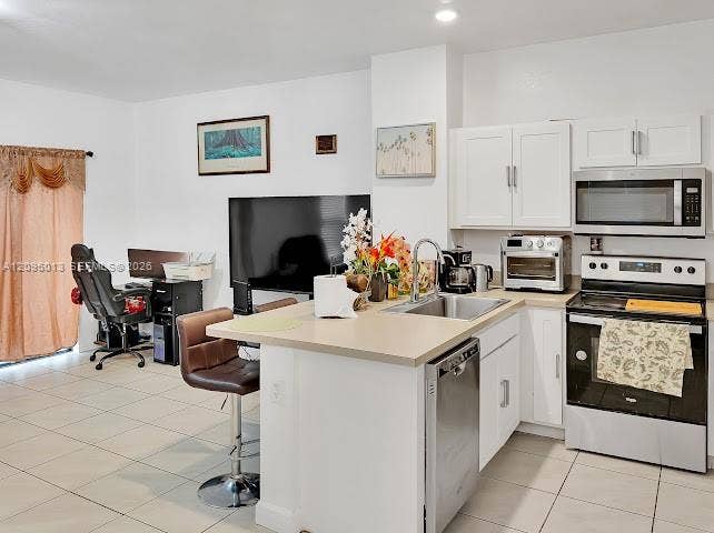 Kitchen featuring white shaker-style cabinetry, solid-surface countertops, a stainless steel undermount sink with a gooseneck faucet, and tile flooring