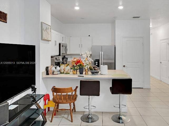Kitchen featuring white cabinetry, solid-surface breakfast bar, recessed lighting, and stainless steel appliances