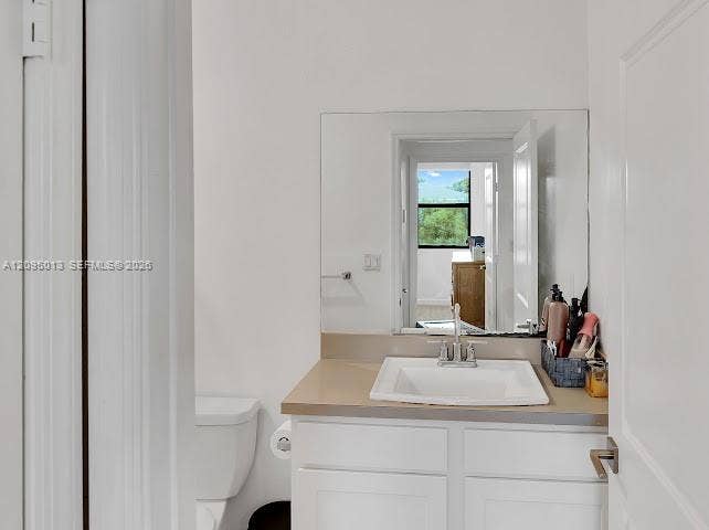 White vanity with a rectangular sink, solid surface countertop, chrome faucet, and expansive wall-mounted mirror