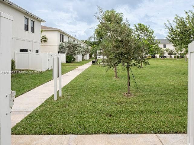 Common green space featuring a concrete pedestrian walkway, mature landscaping, and white privacy fencing