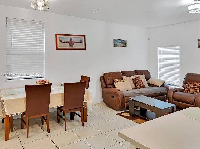 Open-concept interior featuring light-colored tile flooring, multiple windows with horizontal blinds, and geometric flush-mount ceiling lighting