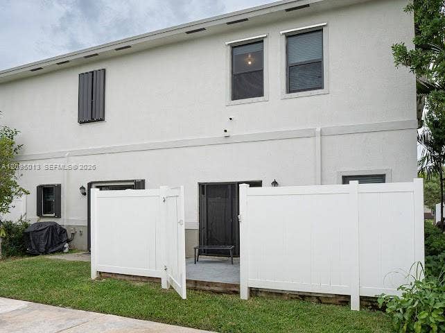 Stucco exterior featuring dual-story windows, privacy-fencing, and a concrete patio