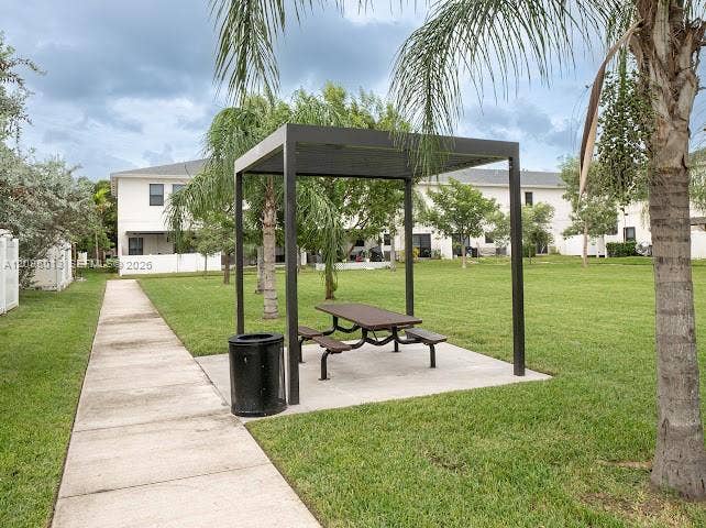 Common green space featuring a concrete walkway, a metal-frame pergola, and mature palm trees