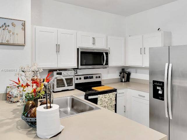 Kitchen featuring white shaker-style cabinetry, solid-surface countertops, stainless steel appliances, and an undermount stainless steel sink