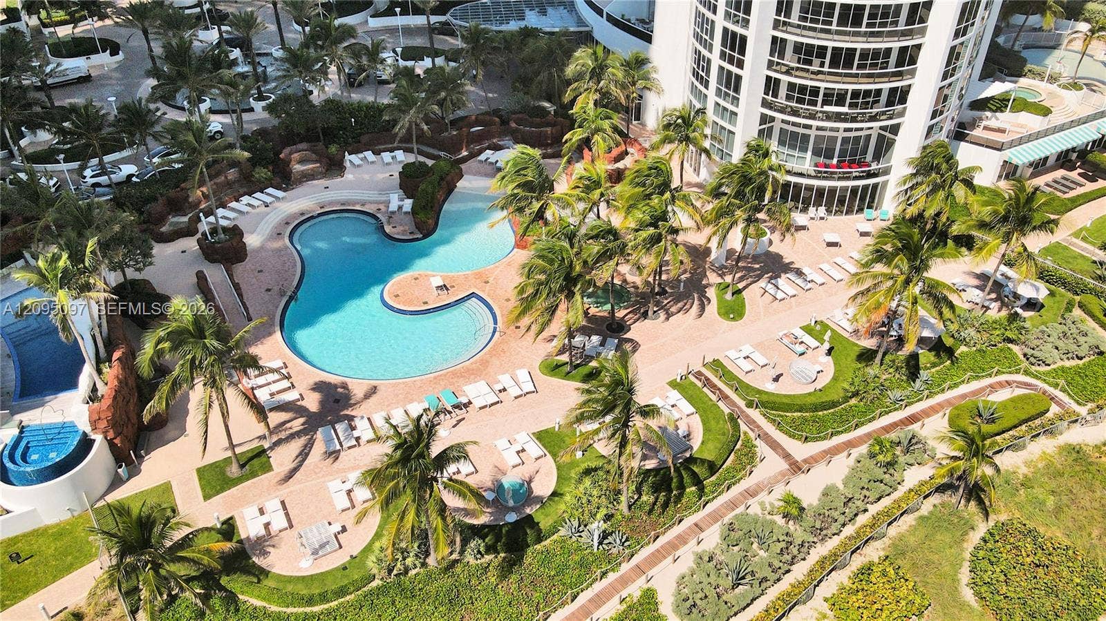 18201 Collins Avenue, #1407, Sunny Isles Beach, FL 33160 Aerial view of a high-rise building featuring a free-form swimming pool, integrated spa, paved sun deck, and tropical landscaping