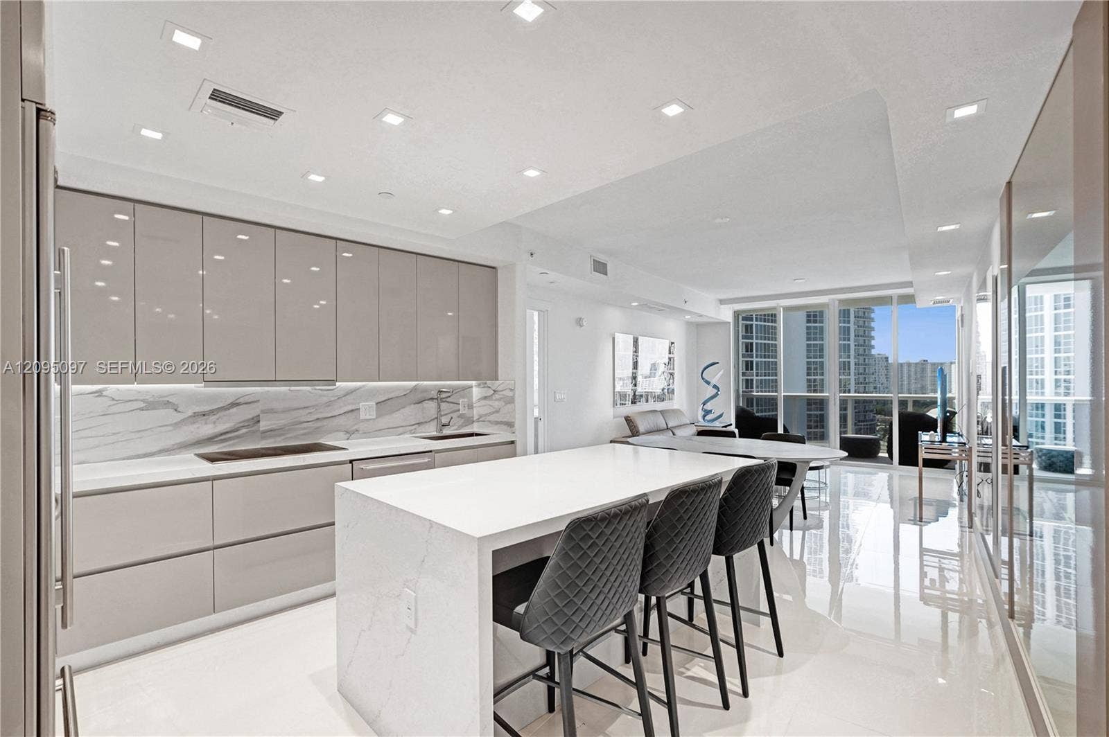 18201 Collins Avenue, #1407, Sunny Isles Beach, FL 33160 Contemporary kitchen featuring high-gloss cabinetry, a waterfall-edge stone island, stone-pattern backsplash, polished tile flooring, and recessed ceiling lighting