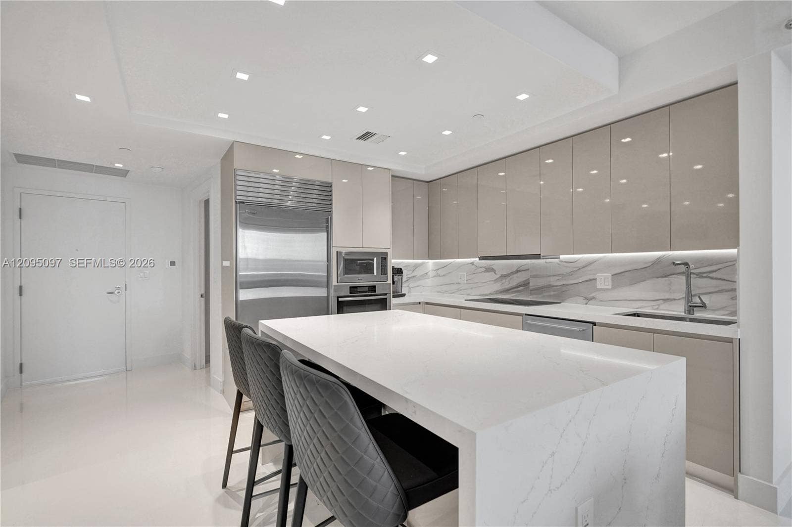 18201 Collins Avenue, #1407, Sunny Isles Beach, FL 33160 Contemporary kitchen featuring high-gloss cabinetry, a waterfall-edge quartz island, under-cabinet lighting, integrated stainless steel appliances, and stone-finish backsplash