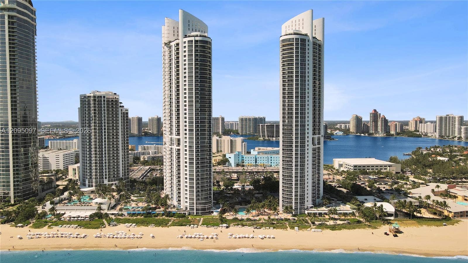 18201 Collins Avenue, #1407, Sunny Isles Beach, FL 33160 High-rise residential towers featuring glass-curtain facades, deep-set private balconies, and direct beachfront access with immediate proximity to coastal waterways