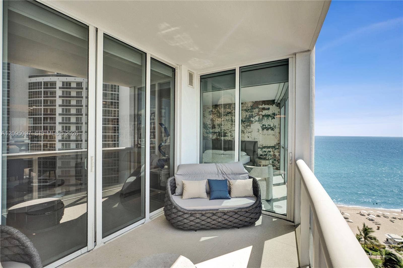 18201 Collins Avenue, #1407, Sunny Isles Beach, FL 33160 Private balcony featuring expansive floor-to-ceiling glass sliding doors, neutral-toned concrete flooring, and a sleek glass-panel railing, set against a direct ocean backdrop