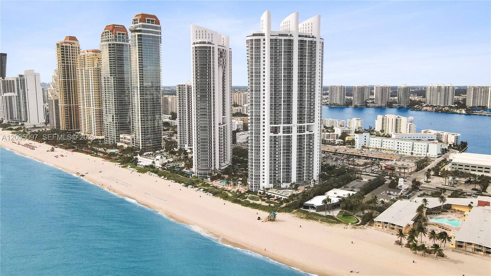 18201 Collins Avenue, #1407, Sunny Isles Beach, FL 33160 Coastal high-rise buildings situated directly on a sandy shoreline, featuring floor-to-ceiling glass facades and proximity to the Atlantic Ocean