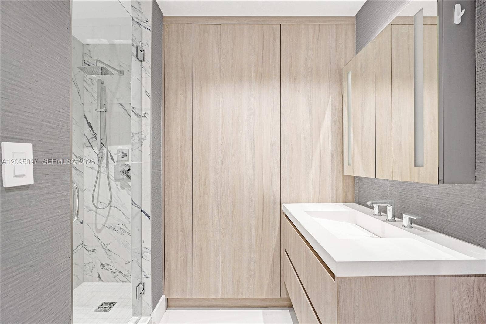 18201 Collins Avenue, #1407, Sunny Isles Beach, FL 33160 Bathroom featuring floor-to-ceiling wood-finish cabinetry, a floating vanity with an integrated basin, a walk-in shower with a rain-style showerhead, and wall-surround tile with a veined pattern