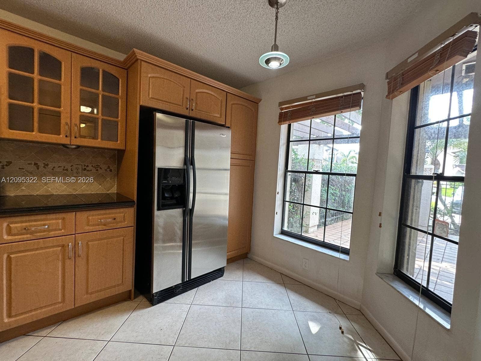 10061 SW 137th Place, Miami, FL 33186 Kitchen featuring wood cabinetry with glass-front display panels, stainless steel side-by-side refrigerator, tile flooring, and dual windows with natural light