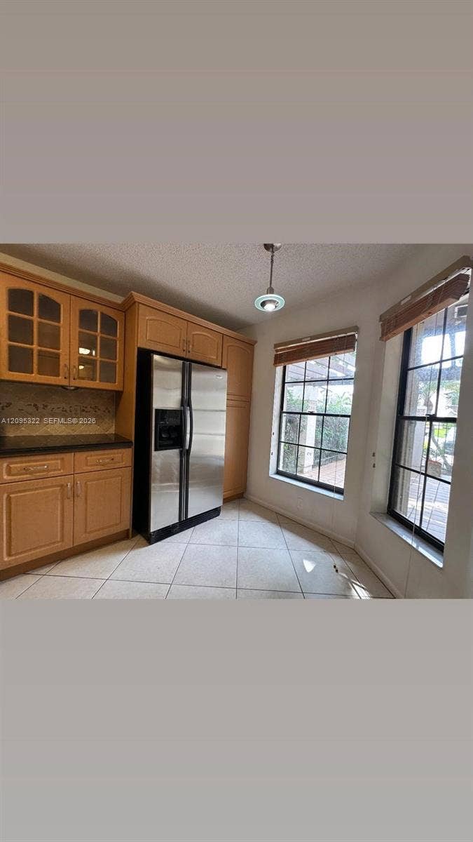 10061 SW 137th Place, Miami, FL 33186 Kitchen featuring wood cabinetry with glass-panel upper doors, stone-finish countertops, stainless steel side-by-side refrigerator, tile flooring, and windows with integrated grilles