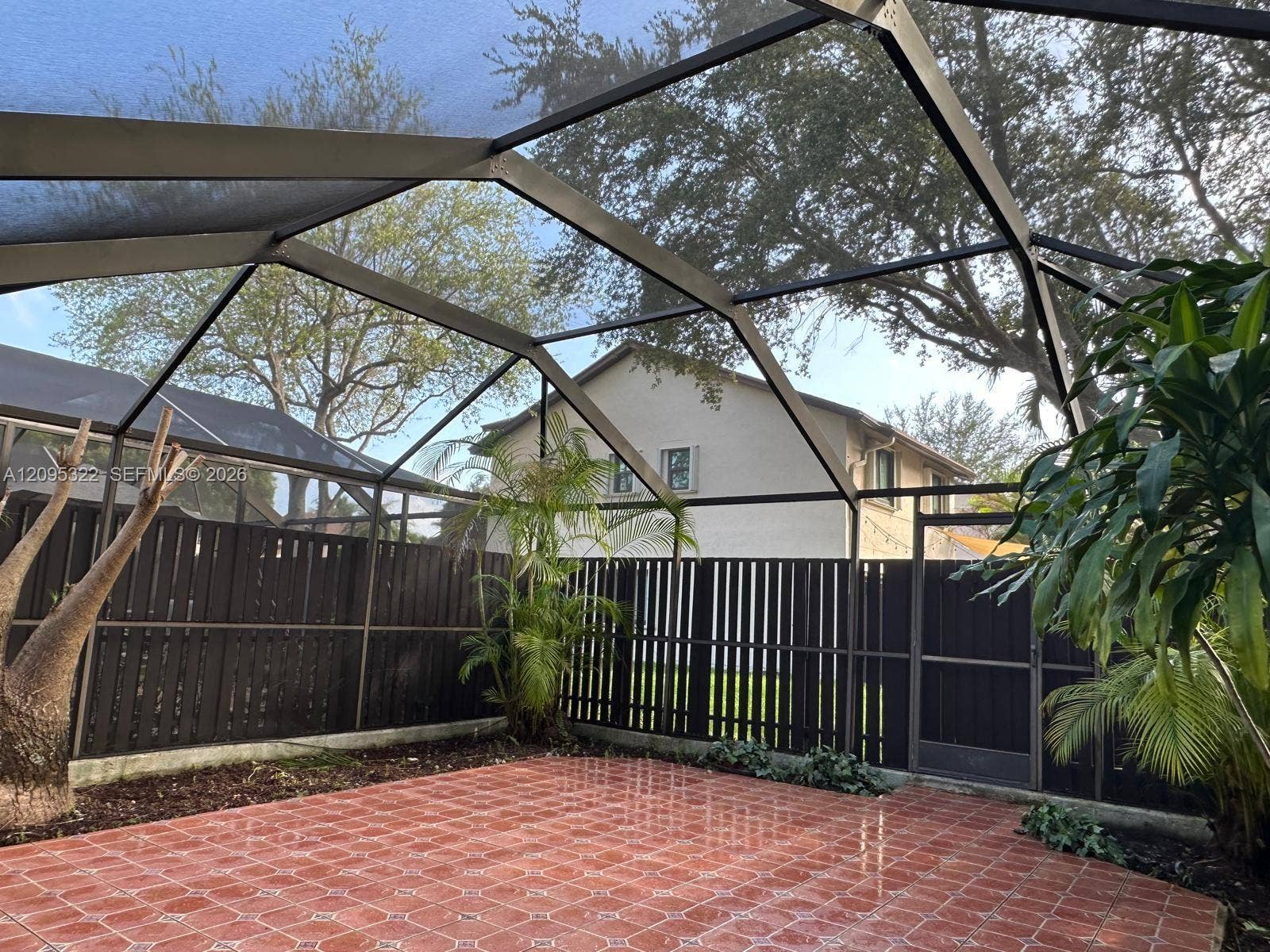 10061 SW 137th Place, Miami, FL 33186 Screen-enclosed patio featuring decorative ceramic tile flooring, a dark-toned vertical slat privacy fence, and integrated landscaping