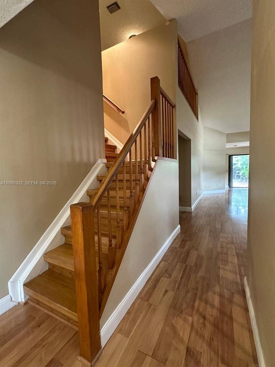 10061 SW 137th Place, Miami, FL 33186 Staircase featuring wood treads and a stained wood railing, complemented by wood-finish flooring and a high-vaulted ceiling
