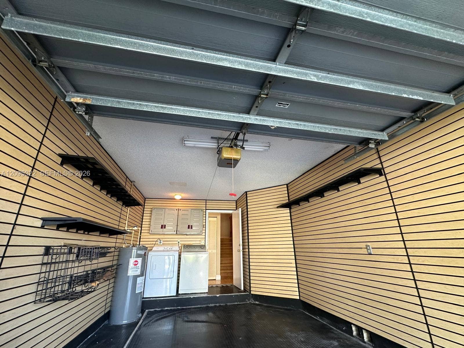 10061 SW 137th Place, Miami, FL 33186 Garage interior featuring wall-mounted slat wall organizational panels, fixed shelving, a water heater, and built-in laundry hookups