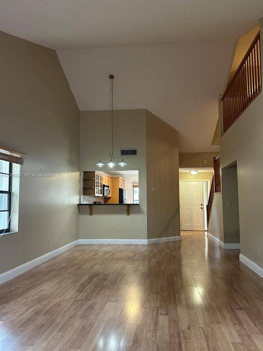 10061 SW 137th Place, Miami, FL 33186 Vaulted ceilings, wood-finish flooring, three-light chandelier, pass-through kitchen opening, and wooden stair railing