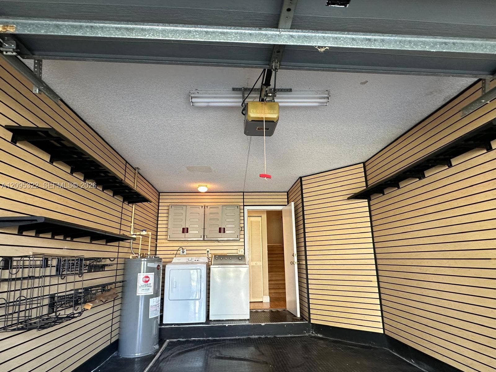 10061 SW 137th Place, Miami, FL 33186 Garage featuring wall-mounted slat storage systems, fixed shelving units, upper cabinetry, and dedicated laundry area with integrated utility connections