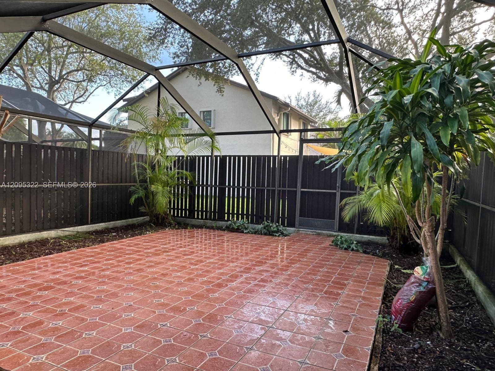10061 SW 137th Place, Miami, FL 33186 Enclosed outdoor patio featuring a screened-in roof, tiled flooring, wood-slat privacy fencing, and a built-in metal gate