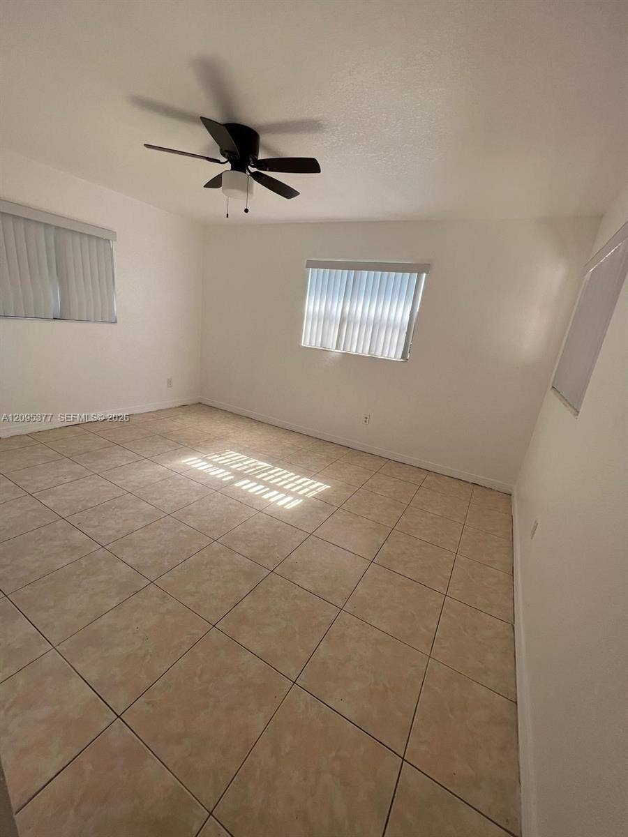 570 NW 41st Street, Miami, FL 33127 Neutral-toned tile flooring, dual windows with vertical blinds, and a matte black ceiling fan with integrated lighting