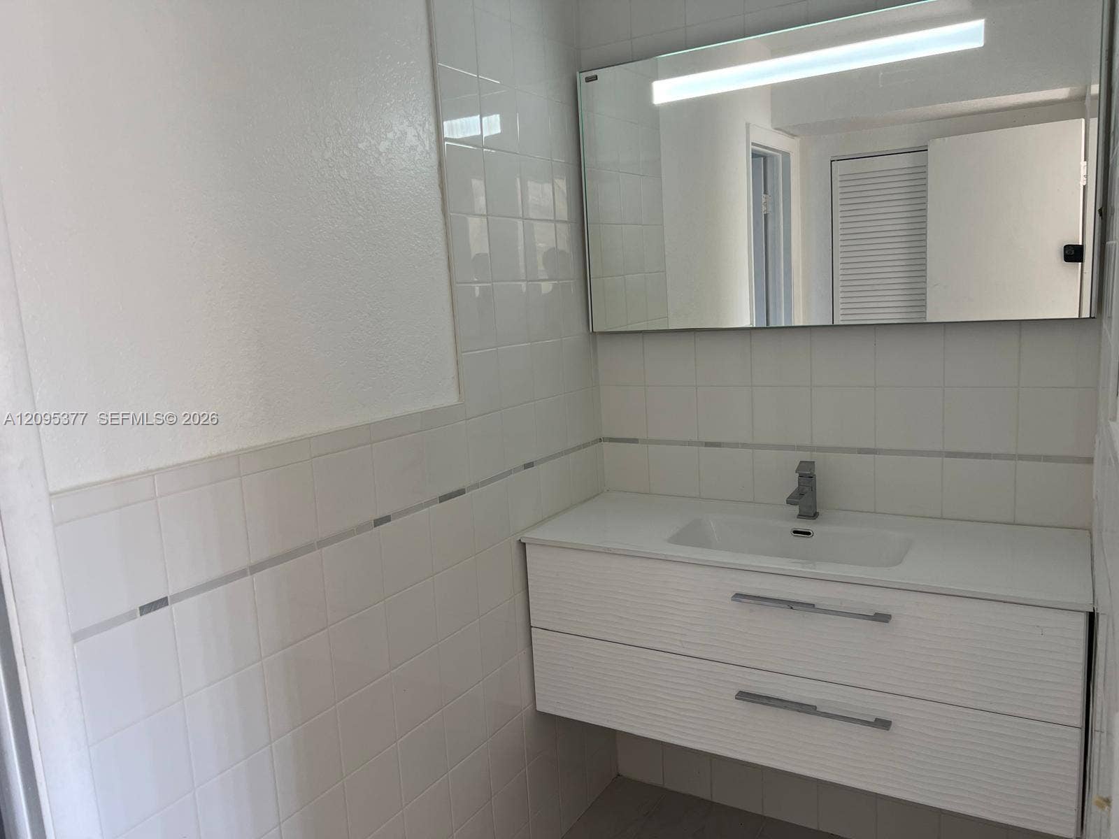 570 NW 41st Street, Miami, FL 33127 Floating vanity with a white countertop and integrated sink, complemented by a large wall-mounted rectangular mirror featuring an integrated light fixture and white tiled walls