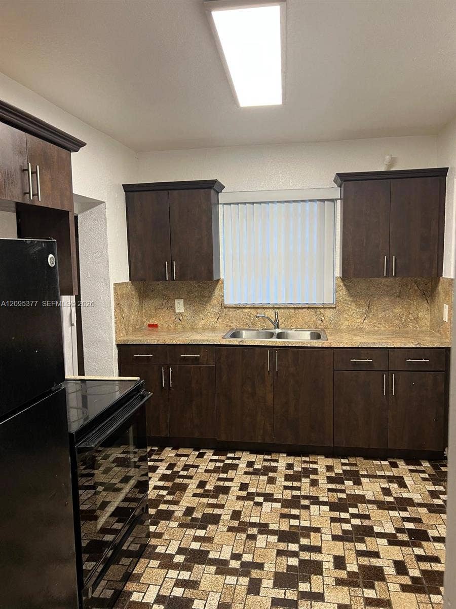 570 NW 41st Street, Miami, FL 33127 Kitchen featuring dark wood-finish cabinetry, stone-texture backsplash, dual-basin stainless steel sink with pull-down faucet, and rectangular flush-mount ceiling lighting