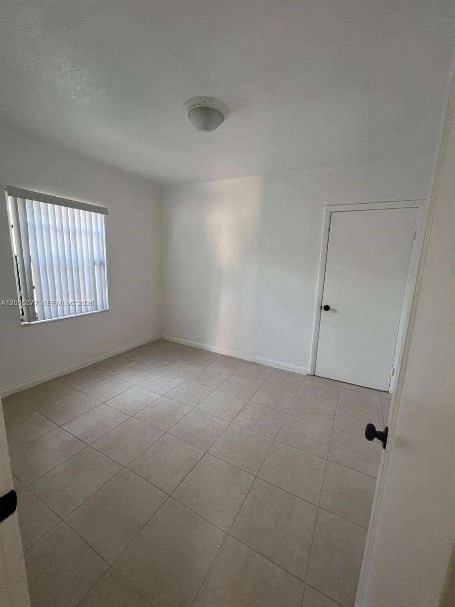 570 NW 41st Street, Miami, FL 33127 Neutral-toned tile flooring, white wall finish, interior door with black hardware, and a single window featuring vertical blinds