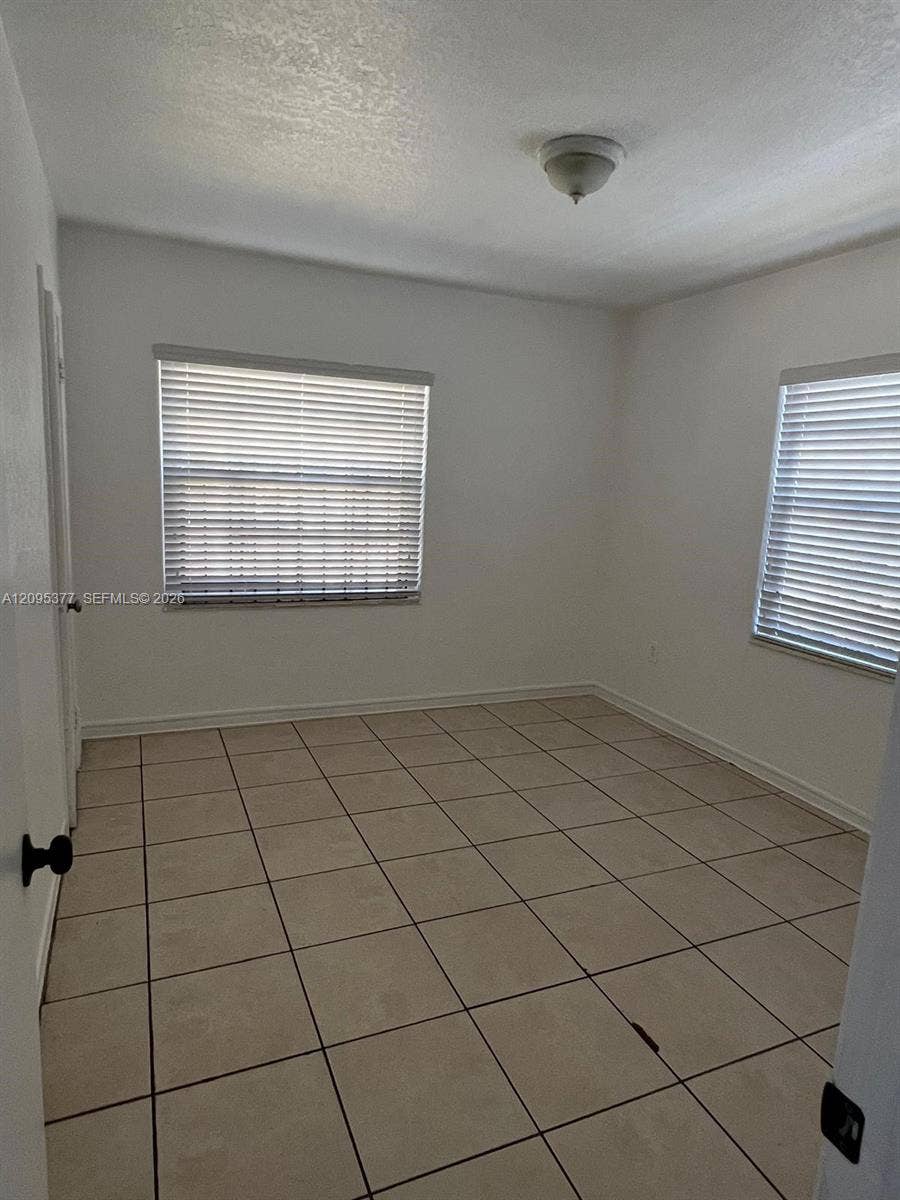 570 NW 41st Street, Miami, FL 33127 Neutral interior featuring light-toned ceramic tile flooring, two windows with horizontal blinds, and a flush-mount ceiling light fixture