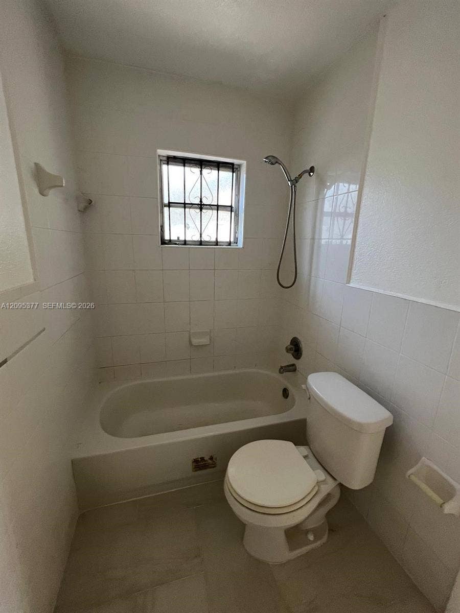 570 NW 41st Street, Miami, FL 33127 Full-height tiled walls, porcelain bathtub with a handheld shower fixture, and a window with security bars