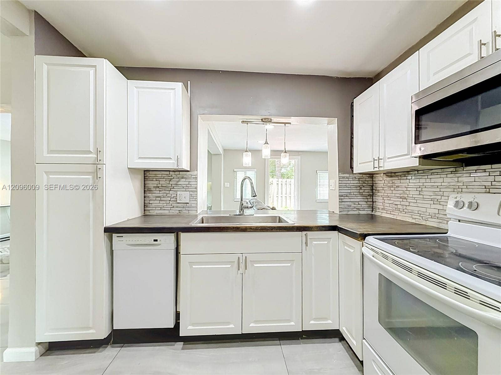 1191 Alabama Avenue, Fort Lauderdale, FL 33312 Kitchen featuring white cabinetry, dark countertops, a stacked-stone tile backsplash, stainless steel sink with pull-down faucet, and white appliances