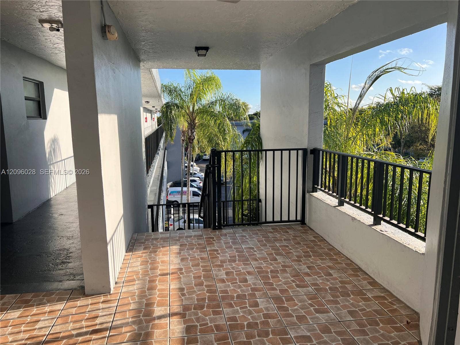 6300 SW 138th Court, #405, Miami, FL 33183 Covered exterior landing featuring stone-patterned tile flooring, black metal railing, and overhead lighting