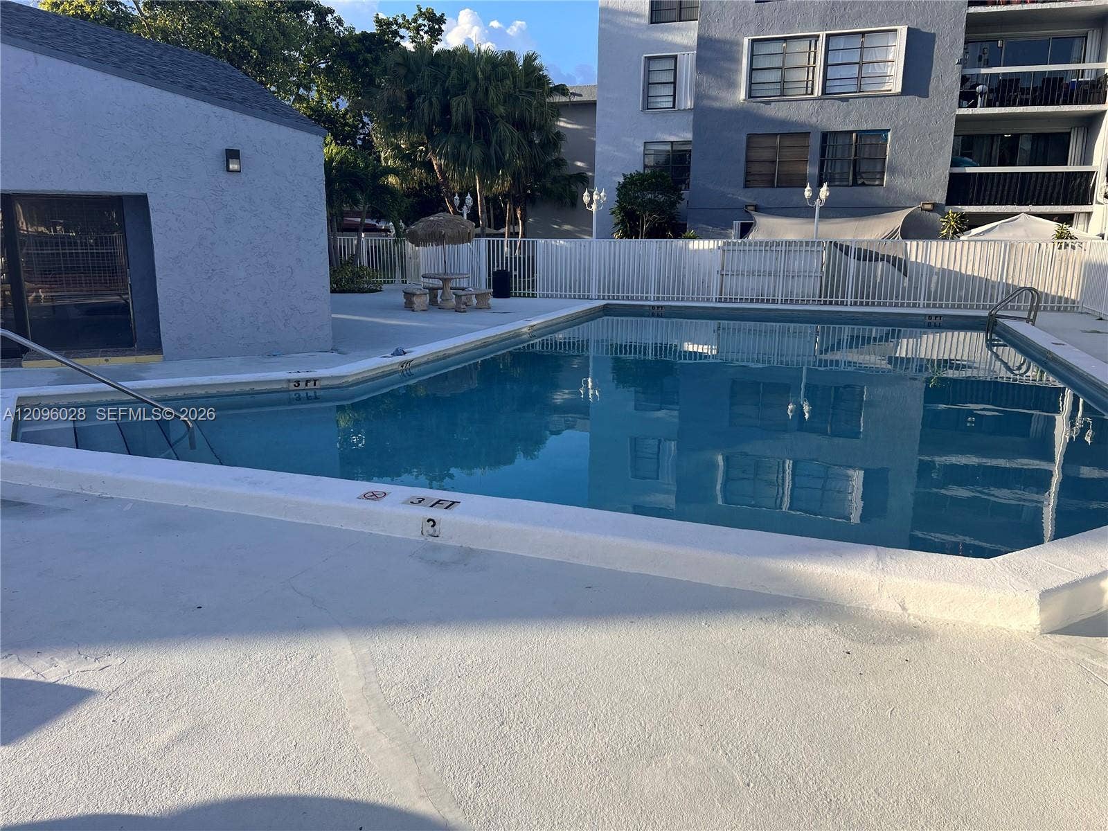6300 SW 138th Court, #405, Miami, FL 33183 In-ground swimming pool featuring a multi-sided basin, metal entry handrails, and a wide concrete deck enclosed by white fencing