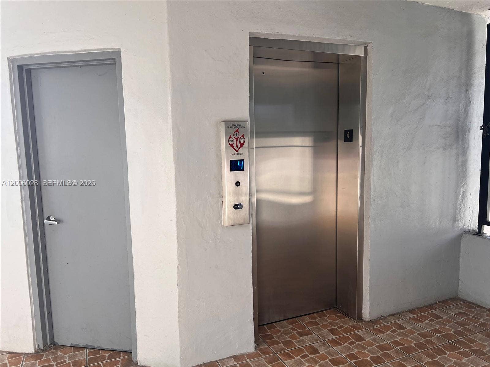 6300 SW 138th Court, #405, Miami, FL 33183 Stainless steel elevator with a digital floor indicator and push-button controls, accompanied by a solid-core door and terracotta-tone tiled flooring