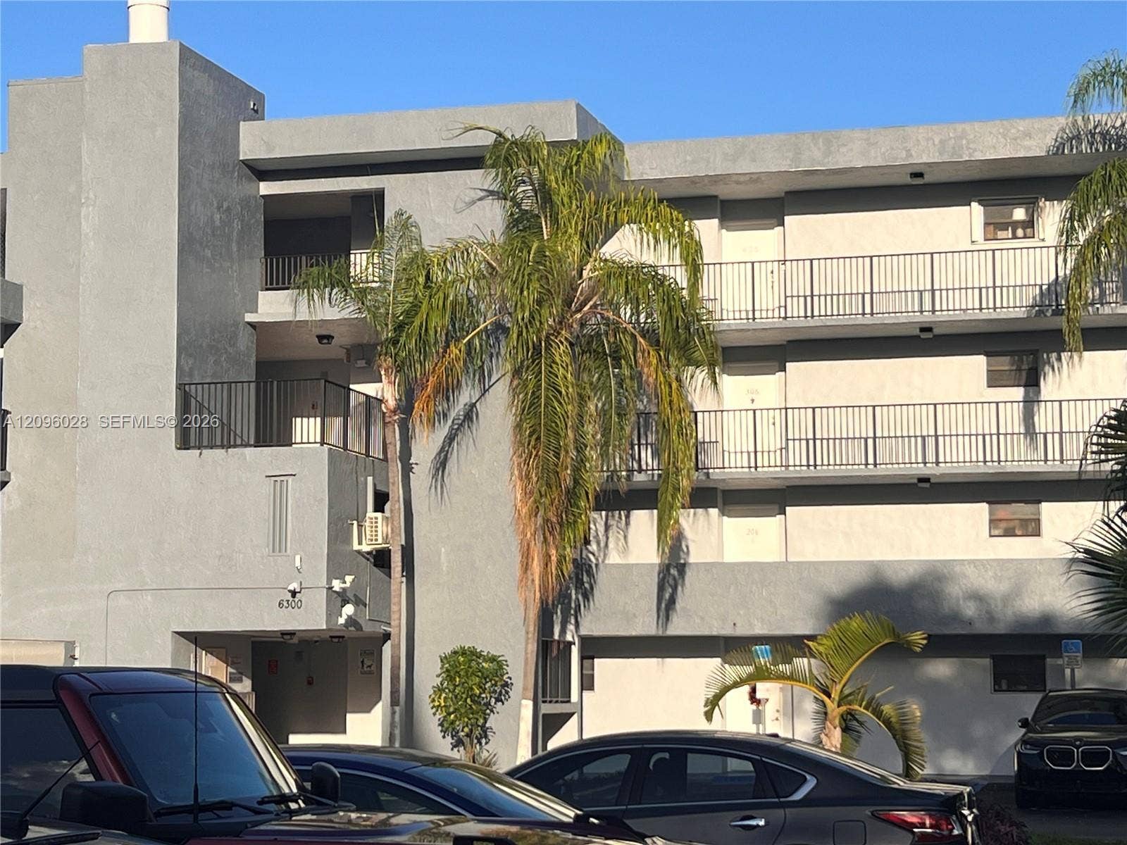 6300 SW 138th Court, #405, Miami, FL 33183 Multi-story exterior featuring a gray stucco facade, private balconies with black metal railings, and mature palm trees
