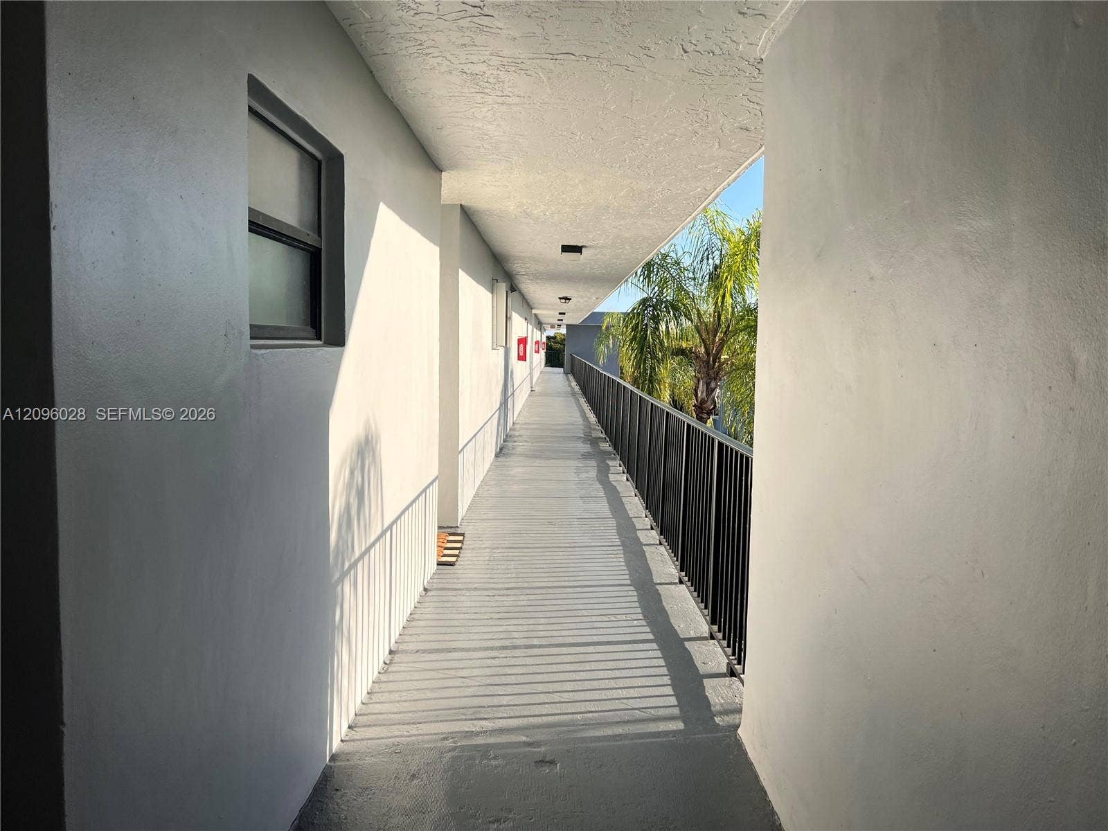 6300 SW 138th Court, #405, Miami, FL 33183 Exterior walkway featuring a painted concrete floor, solid masonry walls, a metal railing, and surface-mounted ceiling light fixtures