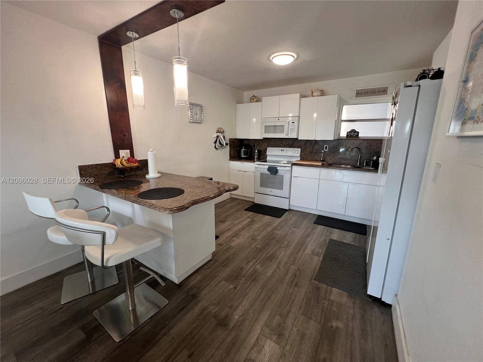 6300 SW 138th Court, #405, Miami, FL 33183 Kitchen featuring white cabinetry, stone-surface breakfast bar, wood-finish flooring, and dual hanging pendant lights