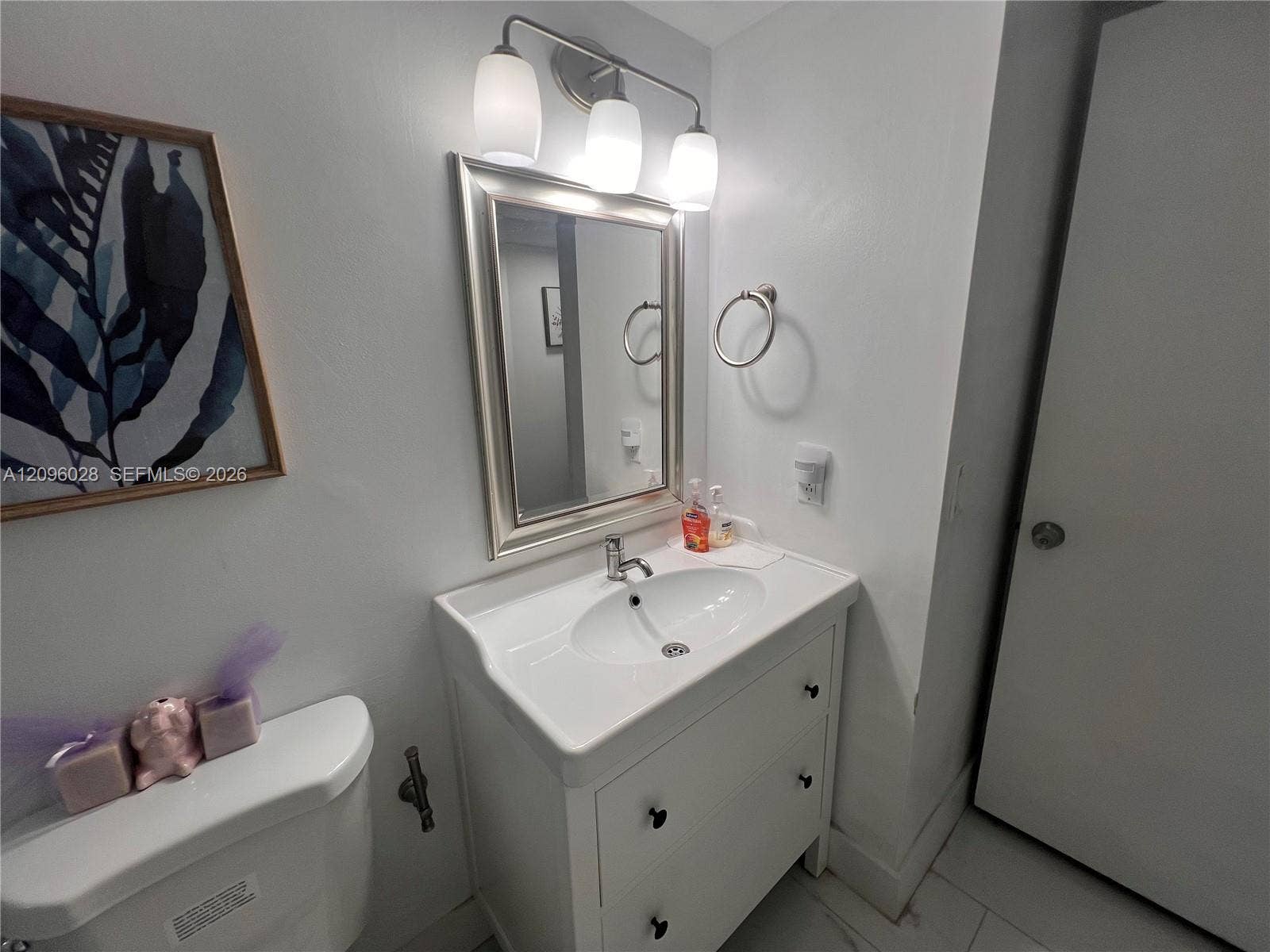 6300 SW 138th Court, #405, Miami, FL 33183 Vanity with integrated porcelain sink, three-light polished chrome fixture, framed wall mirror, and ring towel holder