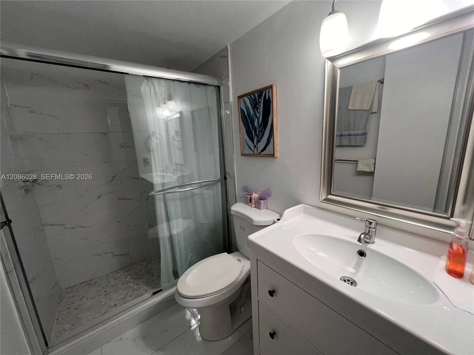 6300 SW 138th Court, #405, Miami, FL 33183 Bathroom featuring a vanity with an integrated sink, polished chrome faucet, framed mirror, walk-in shower with sliding glass doors and wall tile, and large-format tile flooring