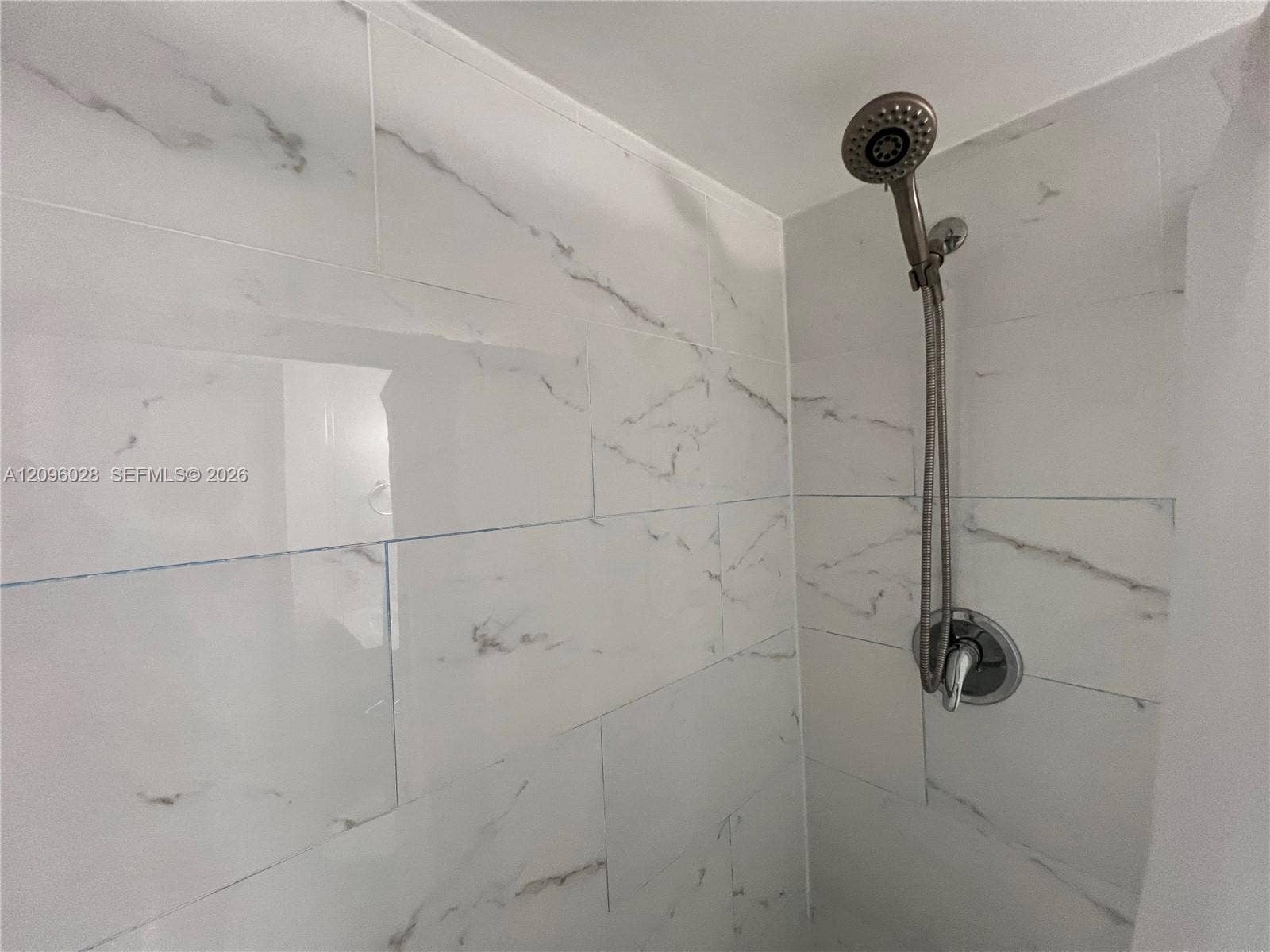 6300 SW 138th Court, #405, Miami, FL 33183 Shower enclosure featuring large-format veined tile surround, adjustable handheld shower head, and single-handle mixing valve