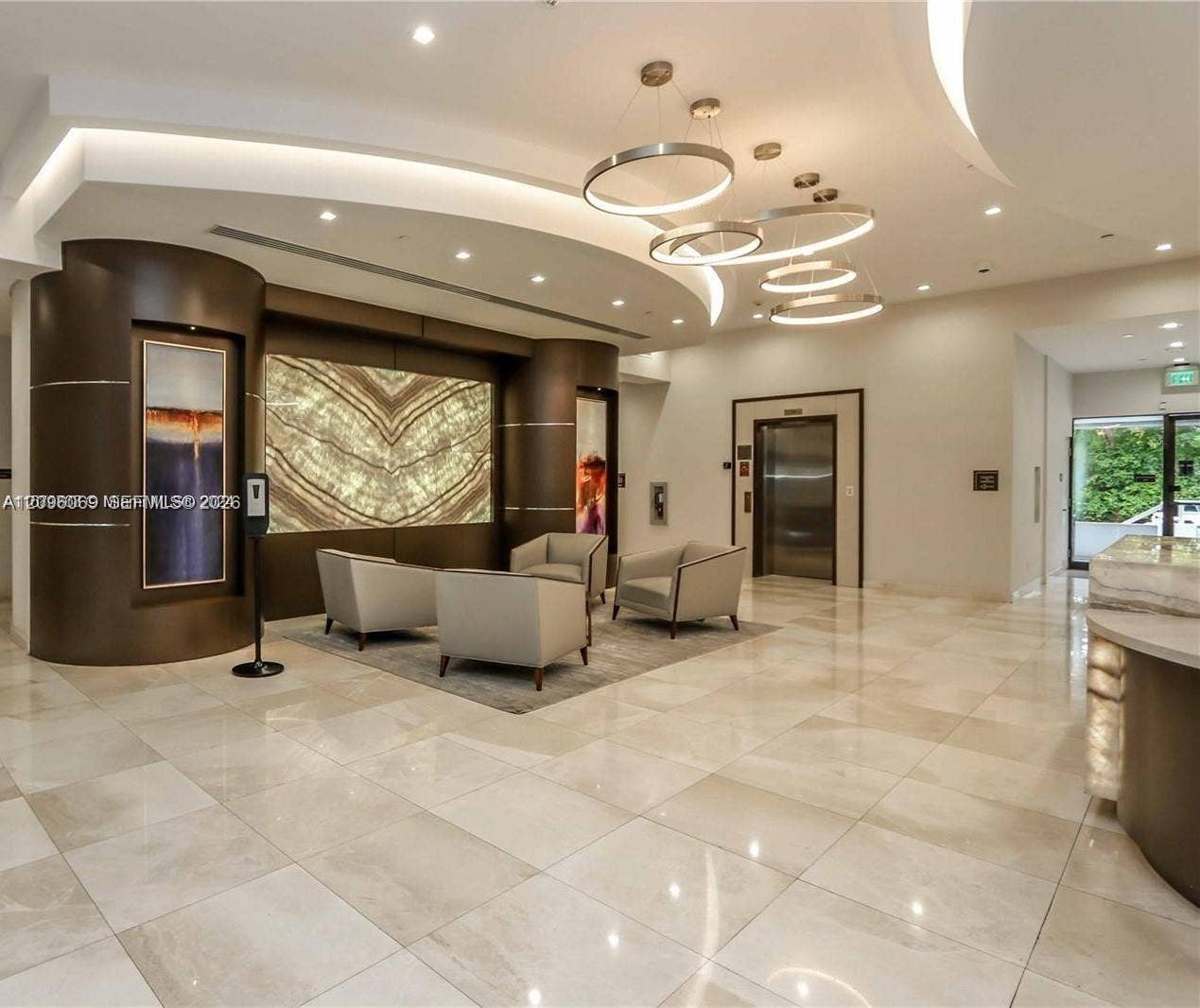 20355 NE 34th Court, #1925, Aventura, FL 33180 Lobby featuring large-format tile flooring, a curved architectural wall accent, backlit stone wall paneling, modern tiered circular pendant lighting, and recessed cove lighting