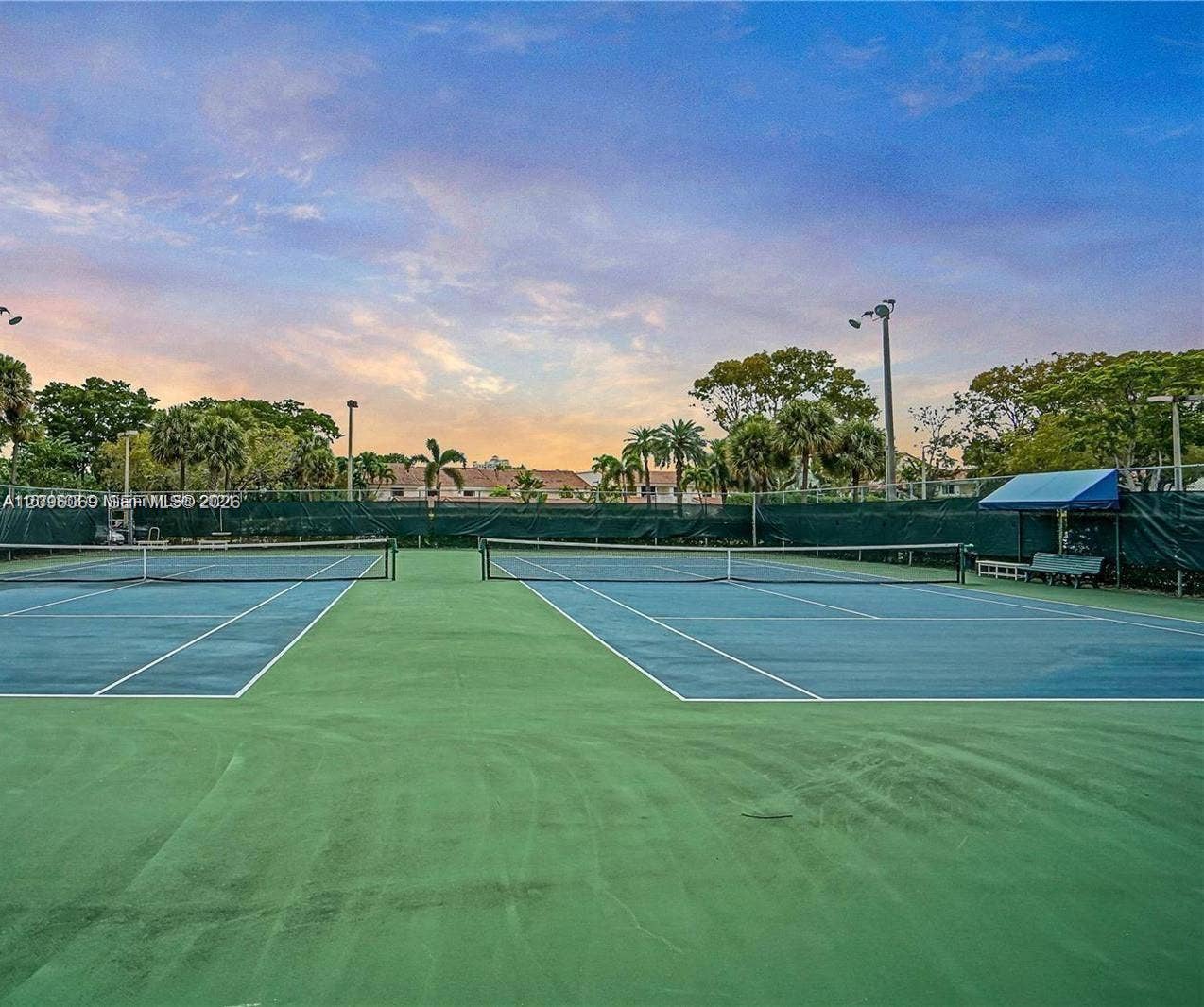 20355 NE 34th Court, #1925, Aventura, FL 33180 Two full-size tennis courts featuring hard-court surfaces, perimeter fencing, overhead lighting, and shaded bench seating