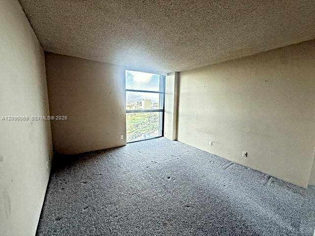 20355 NE 34th Court, #1925, Aventura, FL 33180 Interior room featuring neutral wall finishes, textured ceiling, carpeted flooring, and a large floor-to-ceiling window
