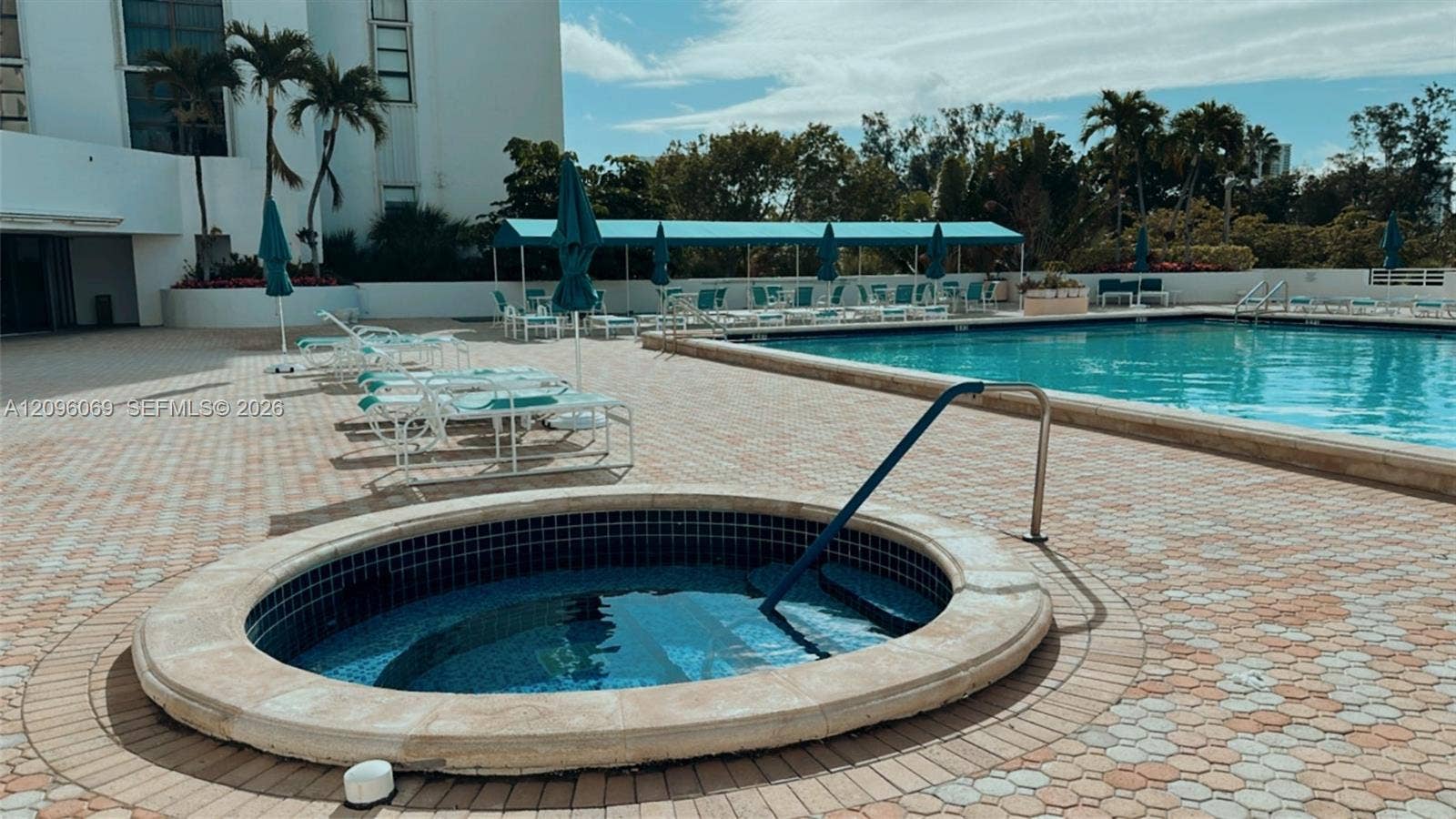 20355 NE 34th Court, #1925, Aventura, FL 33180 In-ground pool and circular spa featuring tile finishes, metal safety railings, and brick-patterned paved decking