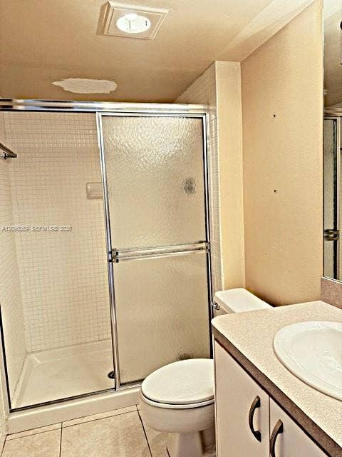 20355 NE 34th Court, #1925, Aventura, FL 33180 Shower enclosure with textured glass sliding doors and white tiled walls, paired with a vanity featuring a neutral countertop, integrated sink, and cabinetry with dark hardware