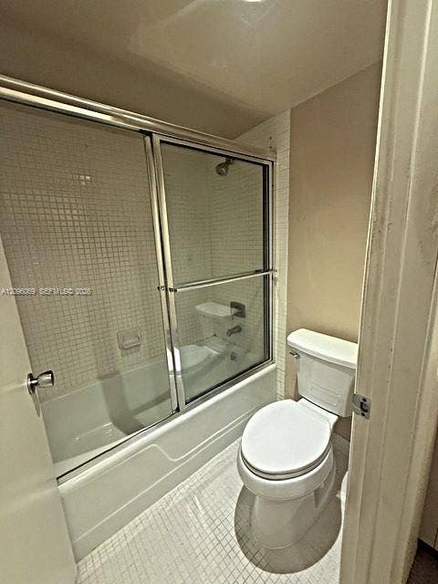 20355 NE 34th Court, #1925, Aventura, FL 33180 Bathroom featuring a shower-tub combination with a glass sliding enclosure, white mosaic wall tile, and a standard-height toilet