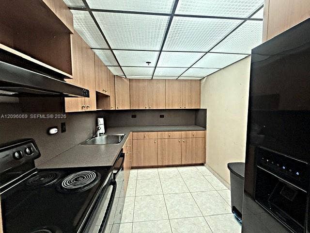 20355 NE 34th Court, #1925, Aventura, FL 33180 Kitchen featuring wood-finish cabinetry, neutral solid-surface countertops, a stainless steel undermount sink, integrated black appliances, and a grid-panel drop ceiling
