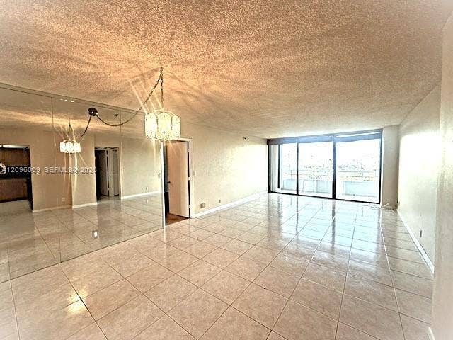 20355 NE 34th Court, #1925, Aventura, FL 33180 Interior space featuring tile flooring, floor-to-ceiling mirrored wall paneling, multi-panel sliding glass doors, and a decorative chandelier