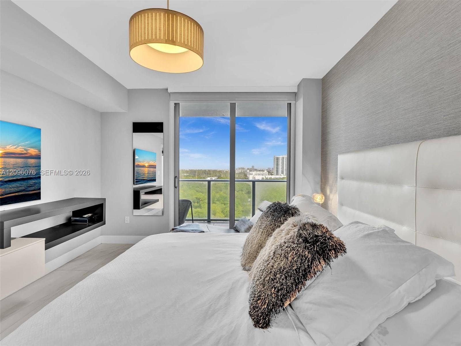16385 Biscayne Boulevard, #1101, North Miami Beach, FL 33160 Floor-to-ceiling glass sliding doors, textured accent wall, drum-style pendant light fixture, built-in cantilevered wall shelf, and balcony with metal railing