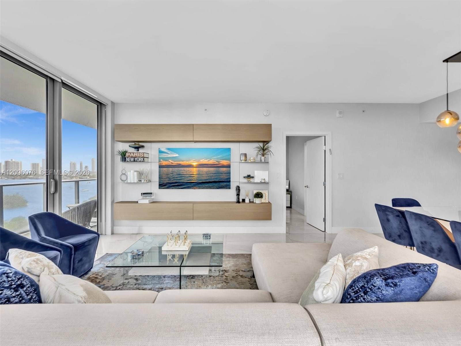 16385 Biscayne Boulevard, #1101, North Miami Beach, FL 33160 Living area featuring floor-to-ceiling glass panel doors, custom built-in wood-finish cabinetry, neutral stone-finish flooring, and pendant lighting