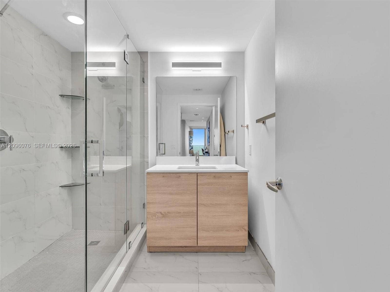 16385 Biscayne Boulevard, #1101, North Miami Beach, FL 33160 Walk-in shower with frameless glass enclosure, wood-finish cabinetry, white countertop with integrated sink, and large-format tile flooring